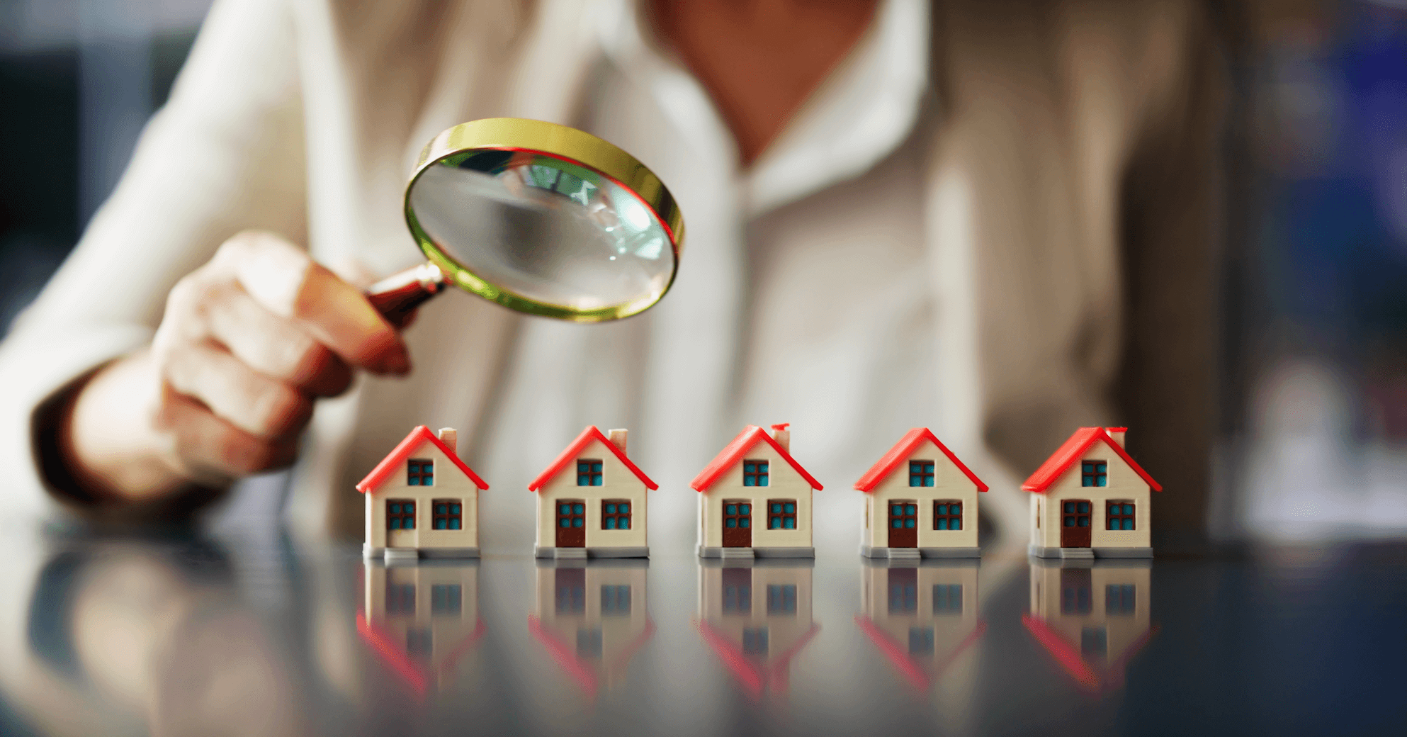 magnifying glass being held up to small house models 